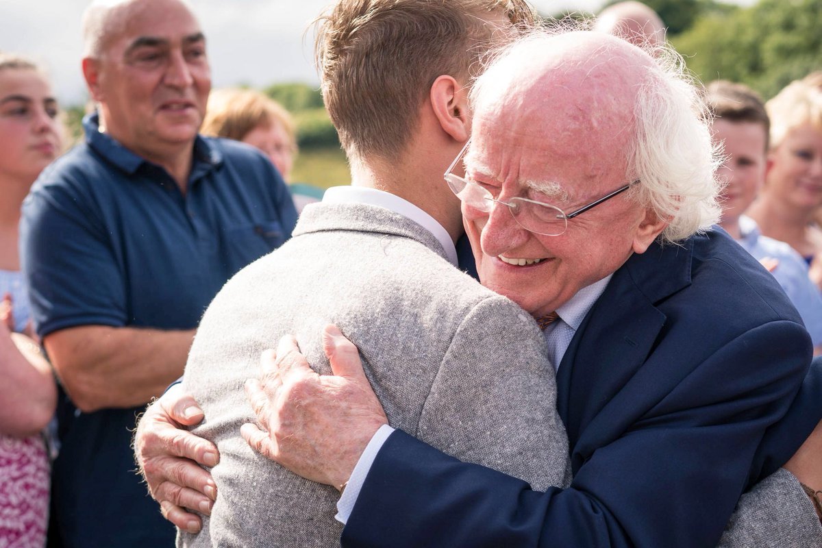 President Michael D Higgins hugging a man. He is in a navy suit, and smiling. There is a crowd of people around, out of focus.