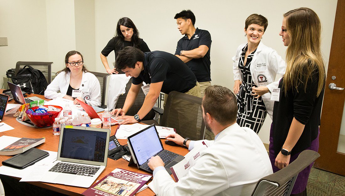 students crowded around a table working on laptops and talking at the competition