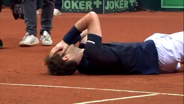 Andy Murray lies on the clay court with his hand covering his face in a moment of intense emotion, while a "JOKER+" advertisement is visible on the wall behind him. The image captures a vulnerable, raw human moment from the tennis star, complementing the post's praise of Murray's human qualities in contrast to the legendary trio of tennis GOATs.