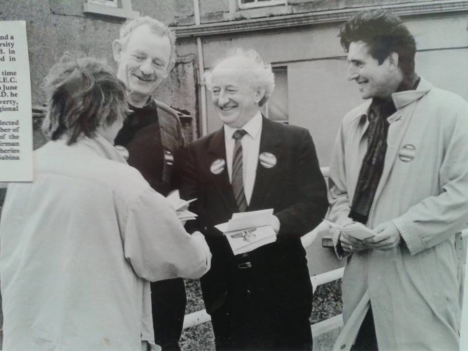 The photograph shows Michael D Higgins in the centre, canvassing with Mick Lally on his left and Gabriel Byrne on his right. They are handing a leaflet to a woman.  The image is monochrome and was taken in the 1980s.