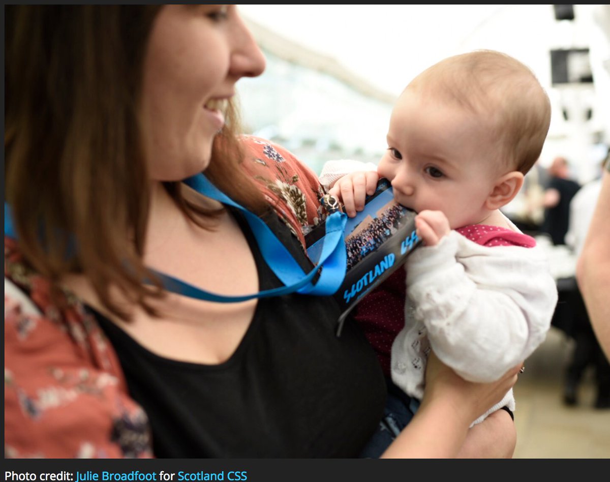 Happy woman holding a baby, while the baby adorably chews on a Scotland CSS conference badge.