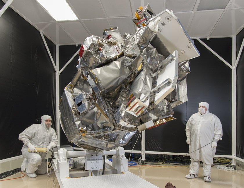 Two people in clean suits look at ICON in a clean room while the spacecraft is held at an angle on a stand.