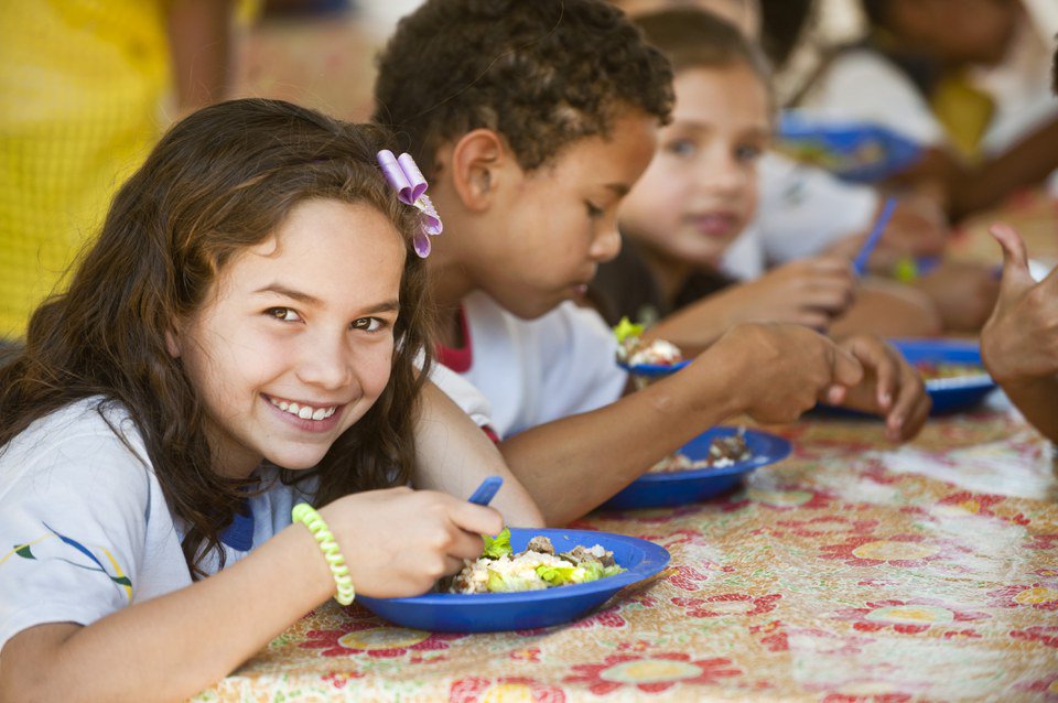 Kids eating. The plates are blue and there's one girl smiling at the camera.