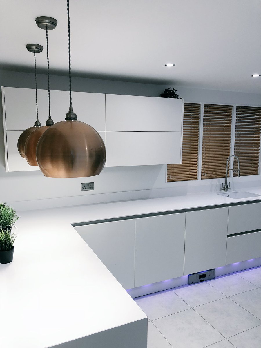 We love this white handleless kitchen with 12mm quartz worktop, brushed copper lights with matching blinds and LED low lights! Available to view in our showroom now. #kitchens#cholsey#showroom