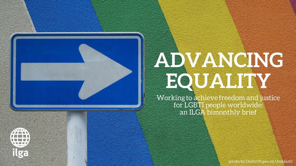 A direction sign in front of a rainbow-painted wall, with an arrow pointing towards a sentence reading "Advancing equality - working to achieve freedom and justice for LGBTI people worldwide: an ILGA bimonthly brief"