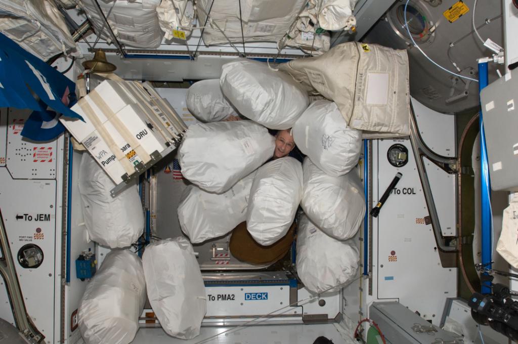 Astronaut inside the International Space Station surrounded by large bags of material