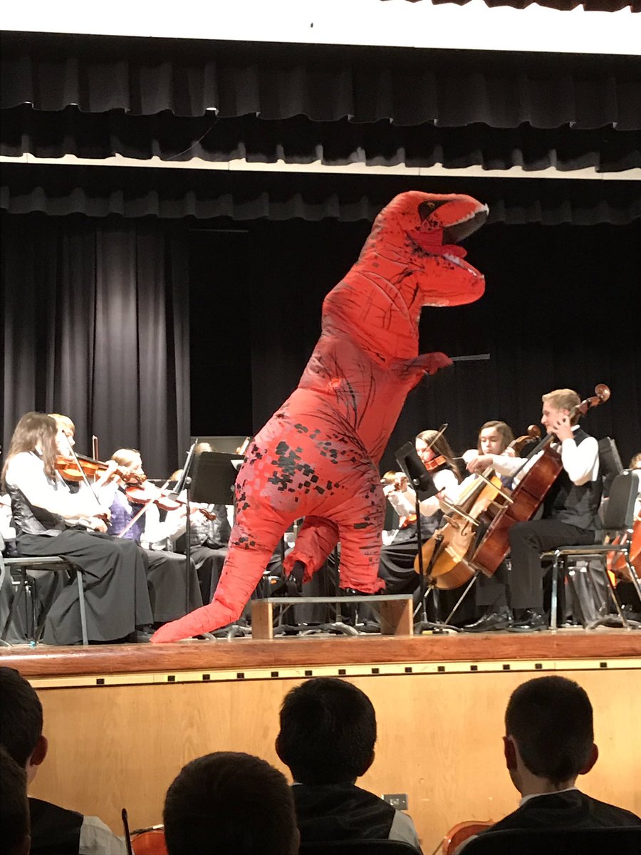evinkm's tweet photo. Tatyana Walters directs the 8th grade choir playing Jurassic Park wearing a dinosaur costume.  She sold it!  Lakeshore students and families love orchestra. Who wouldn’t @ghschools https://t.co/AwaqQHM8RS