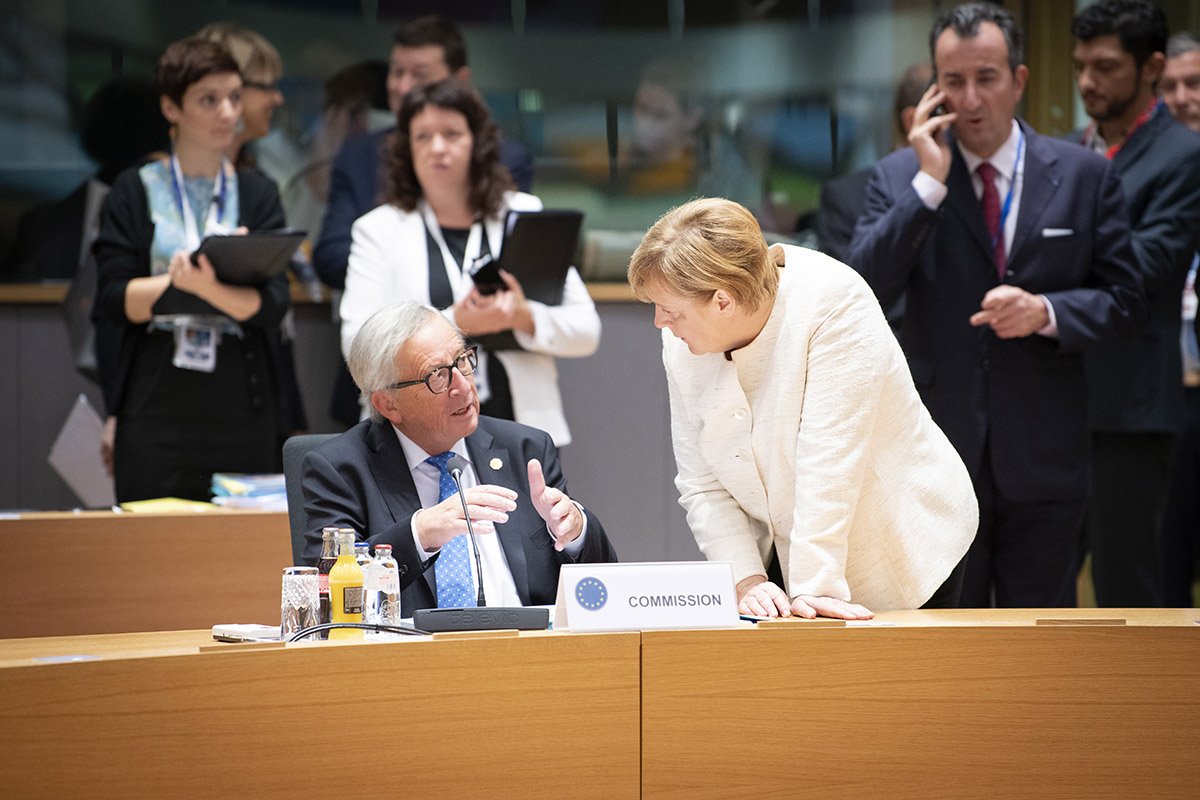 Kanzlerin Merkel beugt sich für ein Gespräch zu Kommissionspräsident Juncker hinab.