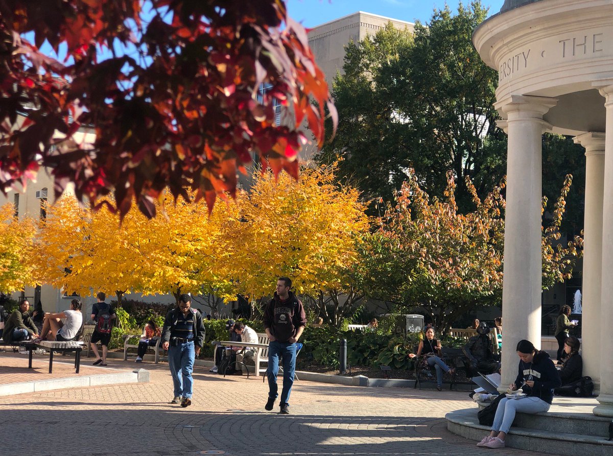 students sitting or walking around Kogan Plaza amidst bright red and yellow foliage