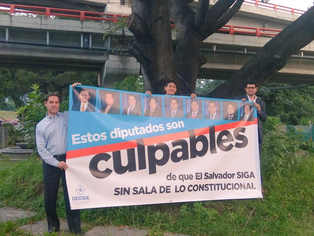 DECIDE_SV's tweet photo. Después de nuestra acción en la Asamblea, ahora estamos en el Redondel Naciones Unidas mostrando en la pancarta los rostros de los responsables de tener entrampada la elección de magistrados a la Corte Suprema de Justicia. 
#ElijanYa #ElijanBien 
#GanaNoQuiereSala https://t.co/Q60VfJlcbA
