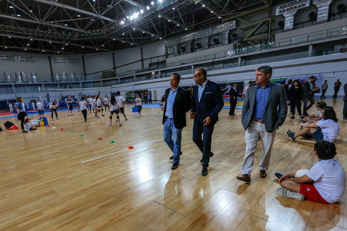 Three men walk through a sports courts full of children.