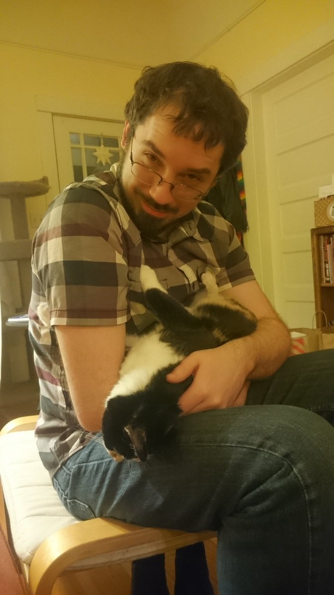 Jamey looking over his glasses with a bemused expression, cuddling a kitty.