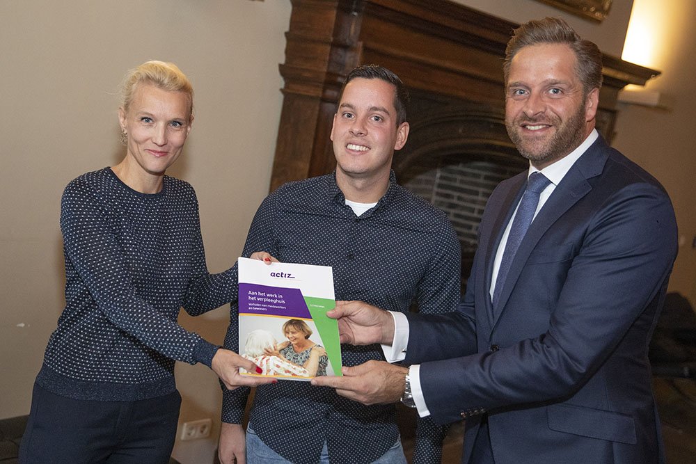 Zorgmedewerkers Jim Landzaad van <a href="/StEykenburg/">Stichting Eykenburg</a> en Roeline Biemond van @Amsta_zorg overhandigen de ActiZ publicatie 'Aan het werk in het verpleeghuis' <a href="/hugodejonge/">Hugo de Jonge</a>. Persoonlijke verhalen over verbeteringen in verpleeghuizen. Lees alle verhalen: bit.ly/2O9o7JL #wijzorgen