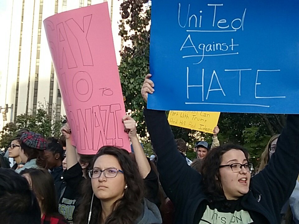 Students gather on Fifth and Dr Soto to await Trump arrival, some with signs.