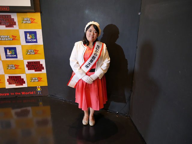 Her sash says なにかの親善大使 ("A goodwill ambassador for something or other")