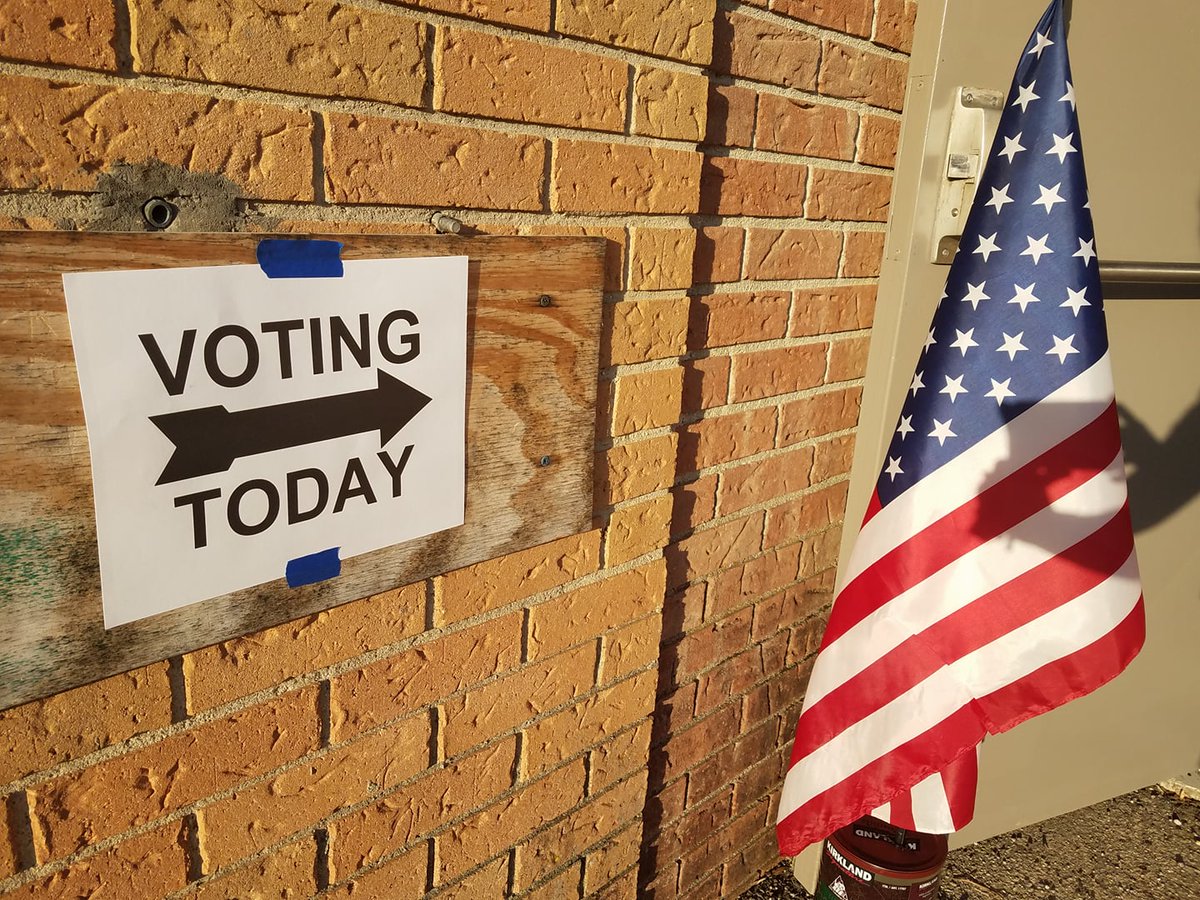 A sign with an arrow says Voting Today and points to an open door next to an American flag