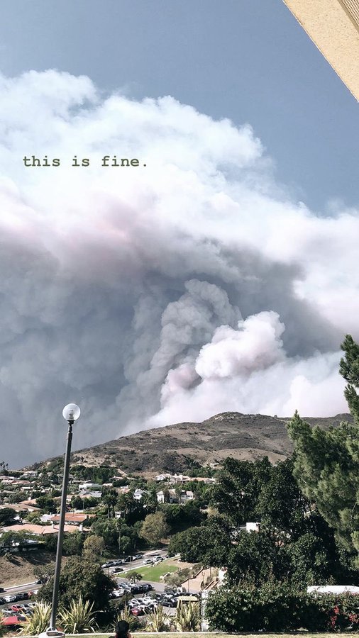 Whitish smoke clouds over a hill & part of college campus w/ caption “this is fine”