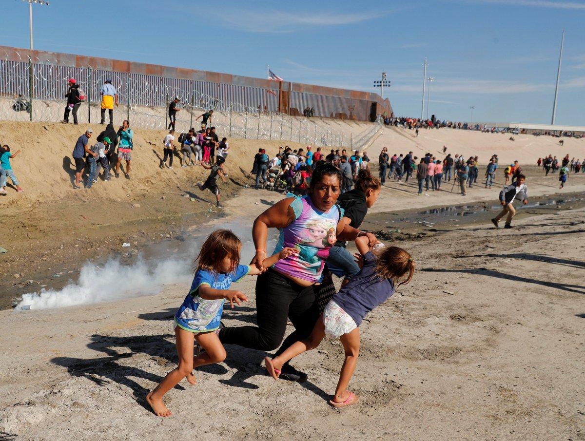 BreakingNews's tweet image. A migrant family, part of a caravan of thousands traveling from Central America to the U.S., run from tear gas in front of the border wall between the U.S. and Mexico at Tijuana on Sunday - @Reuters