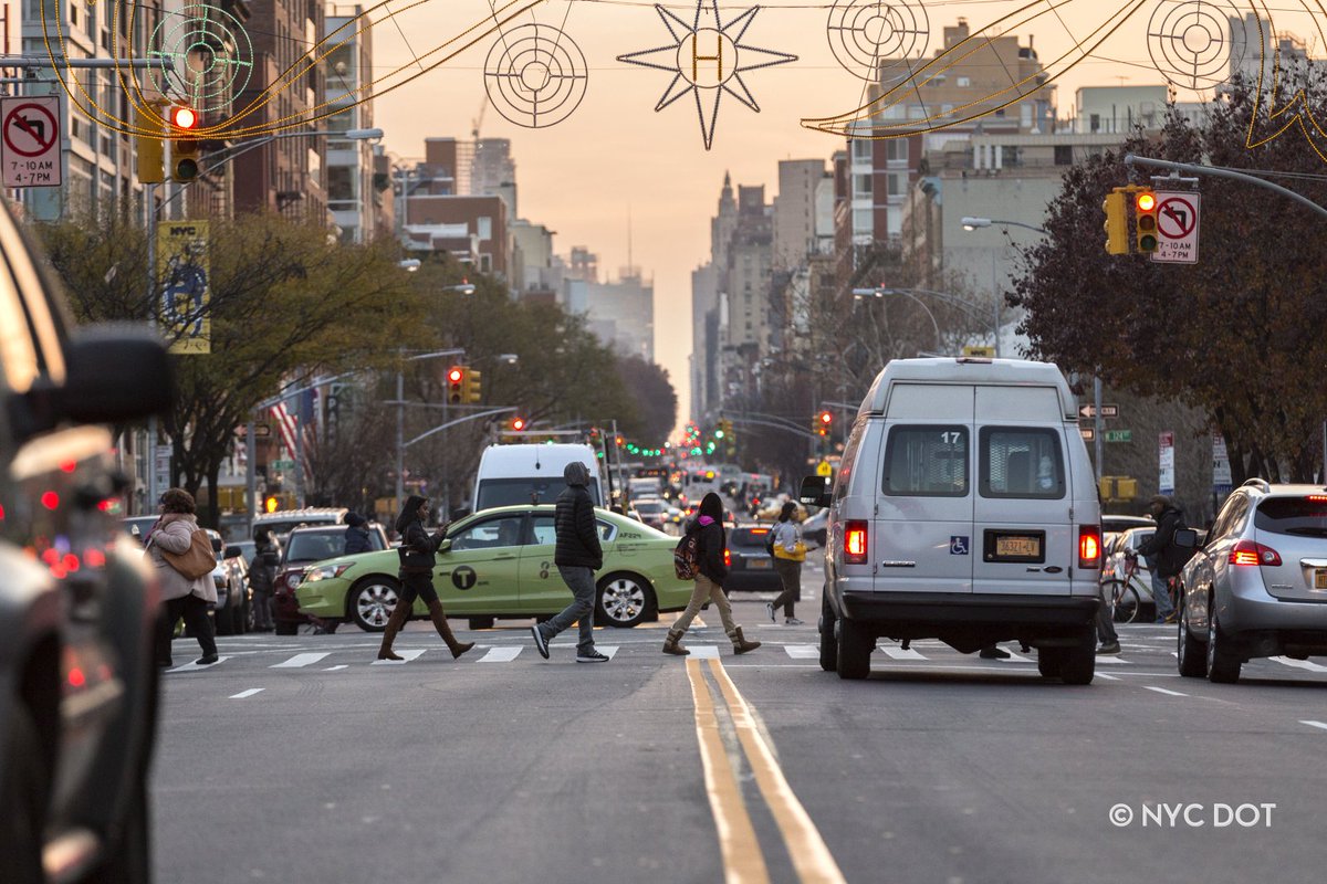 People cross the street while vehicles wait at a red light