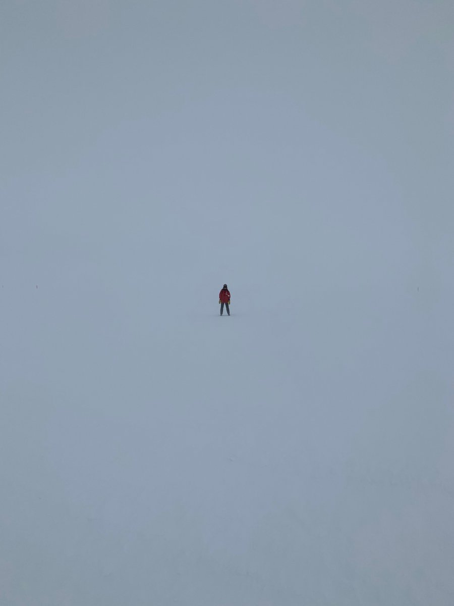 SPTelescope's tweet photo. South Pole white-out!  Poor visibility made it hard to see the telescope from station, very windy, very overcast, and very low contrast.  This is a picture of Jessica on the walk back to station tonight in a sea of white.  #whiteout #southpole #antarctica https://t.co/tl0KBqPivG