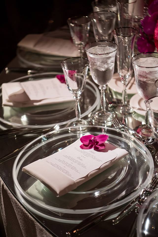 Each guest's place setting showcased a translucent charger plate topped with a menu card and fuchsia orchid blossom as well as silver-rimmed glassware. bit.ly/2CmtDY6 <a href="/whitelilacinc/">White Lilac Inc.</a> <a href="/BobGailEvents/">Allyson Levine</a> <a href="/RevelryDesign/">Revelry Event Design</a> 
(John Solano Photography)