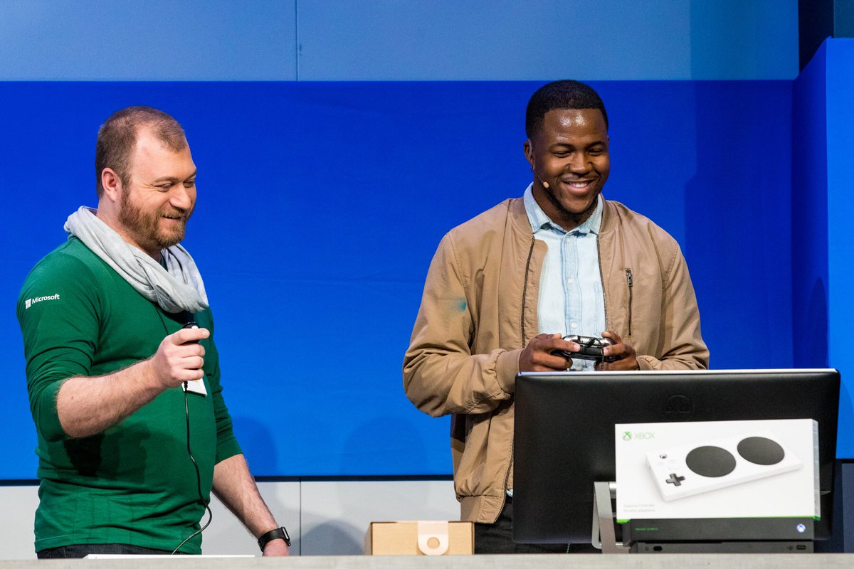 Jamal and Solomon laughing playing forza! Xbox adaptive controller box on the desk and they are holding controllers - Solomon a one handed and Jamal a standard two handed controller.