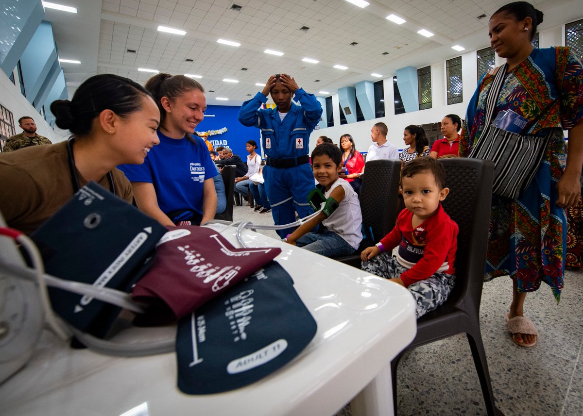 Southcom's tweet photo. All smiles in Colombia: @USNavy Ensign &amp; a volunteer from @USEmbassyBogota check the vital signs of a young patient during the hospital ship #USNSComfort's #EnduringPromise medical support mission in Riohacha, Colombia.  @deptofdefense https://t.co/VpELFEim5w
