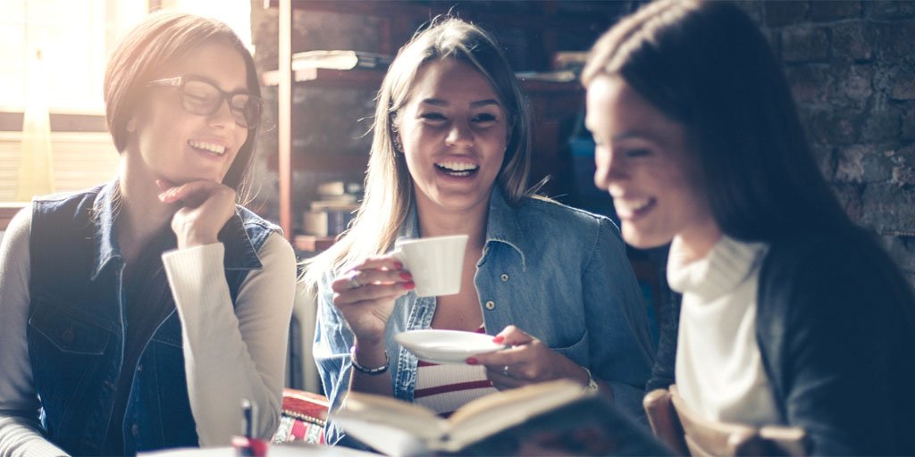 Three young women discuss a book over coffee