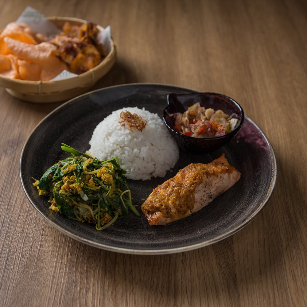 Thick salmon fillet marinated in spices and cooked tenderly is served with steamed rice, crunchy krupuk, fresh urap salad, and potates in balado style on the side adds up to become Ikan Salmon Sambal Sereh. A modern, refined twist of spice-laden Indonesian flavor.