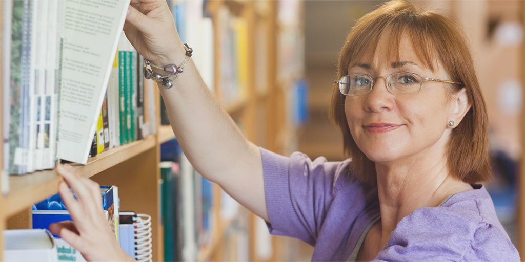 A librarian reaches to take a book off the shelf