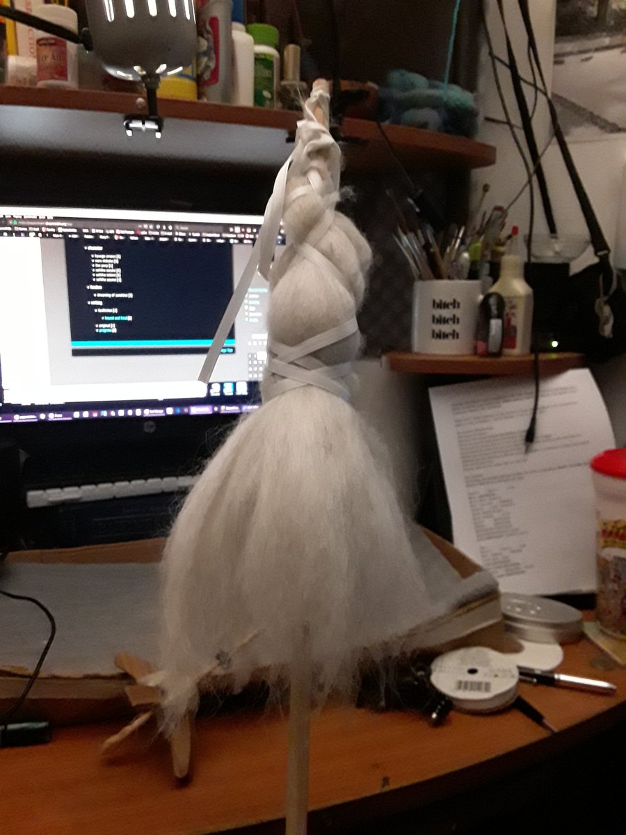 An image of a distaff holding wool for spinning. There is a computer desk in the background