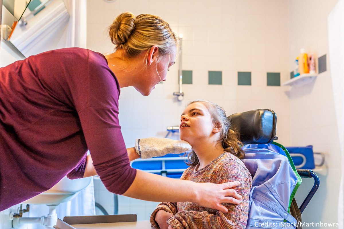 Nurse speaks and holds head of young woman in wheelchair