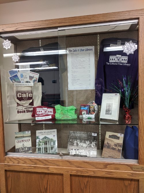UrbanaFree's tweet image. Stopping by the Library today? Stop by the display case to see some Library swag! Pick out a gift for the Library fan in your life! #libraryswag #urbanafree