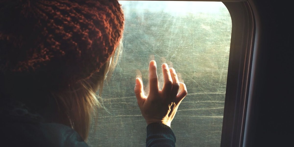 A woman faces a train window, her outstretched hand touching it
