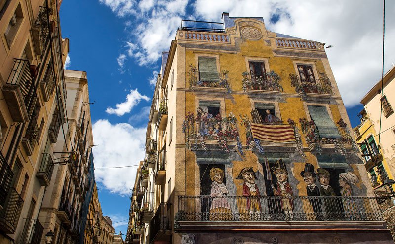 TGNturisme's tweet photo. 🎨 El mural de la plaça dels Sedassos, a la #PartAlta de #Tarragona, és obra del pintor Carles Arola. Representa una façana típica d'una ciutat mediterrània al segle XIX, a la qual va incorporar elements festius i un autoretrat de l'artista. https://t.co/lHOMIrJ7zr