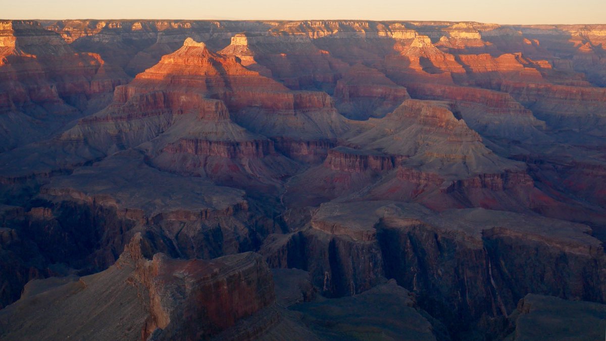 Description: looking down into an expansive desert landscape of peaks, cliffs and valleys, with the last light of orange sunlight about to fade on the horizon.