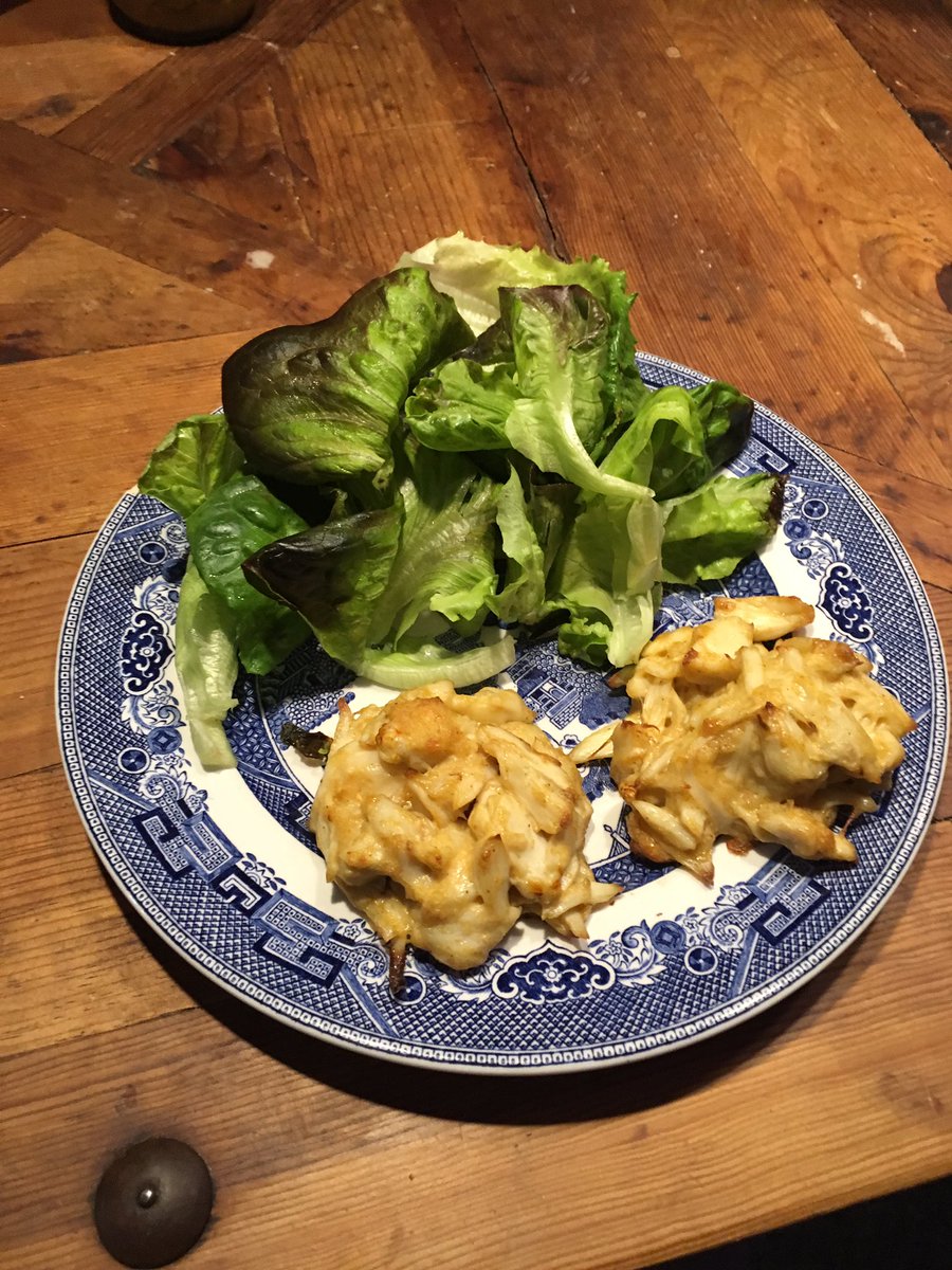 2 crab cakes and a green salad, on a Blue Willow plate on a wooden table.