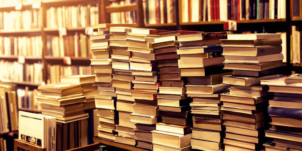 Stacks of books in front of bookshelves in a bookstore or library