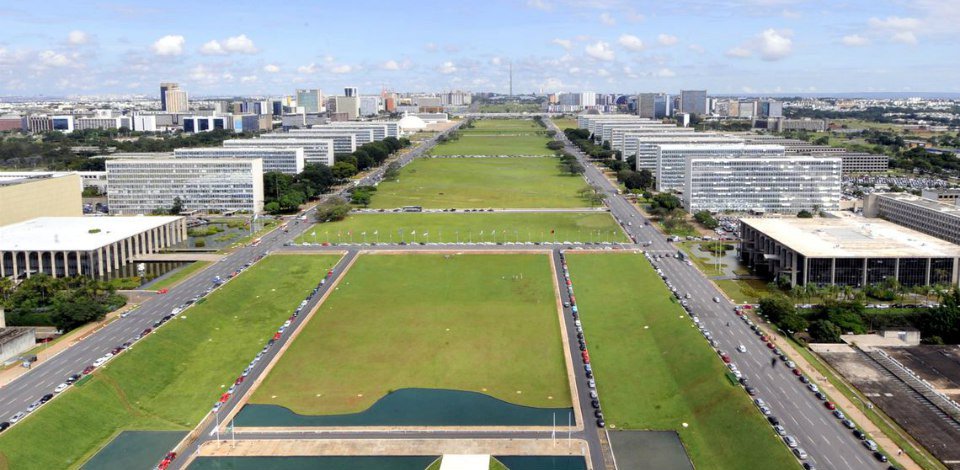 #PraCegoVer: Foto da Esplanada dos Ministérios, em Brasília, vista do alto a partir do prédio do Congresso Nacional. Os prédios são separados por um largo gramado verde no centro. Circularam carros nas avenidas.