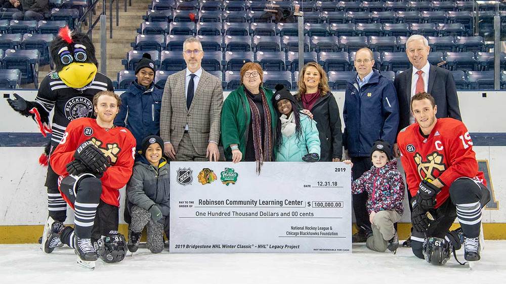 Members of the Chicago Blackhawks kneel with children from the Robinson Community Learning Center near a check for $100,000 while RCLC and NHL staff stand with the Blackhawks mascot behind the check.