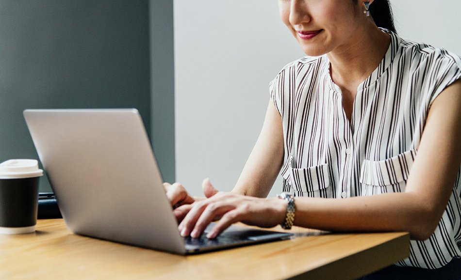 a woman smiling looking down at her laptop, sitting at a desk
