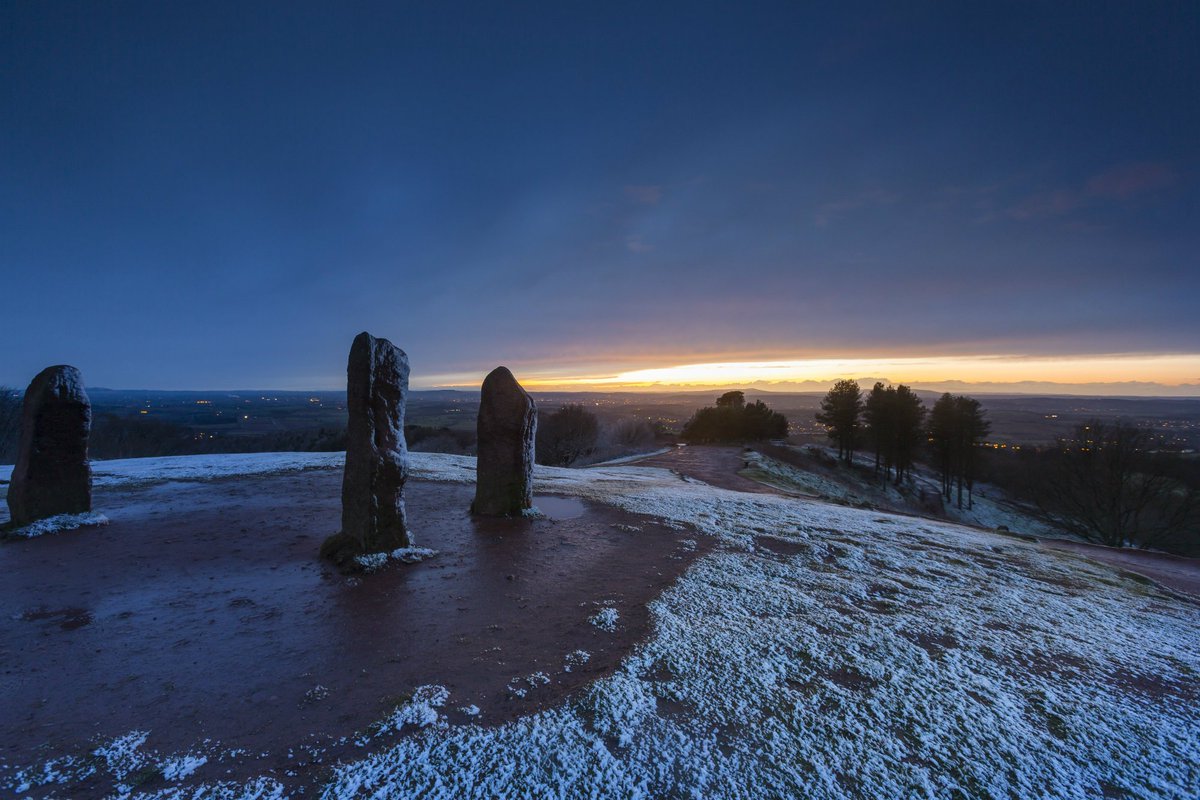 A golden sunrise on the horizon with the Clent Hill stones in the foreground.