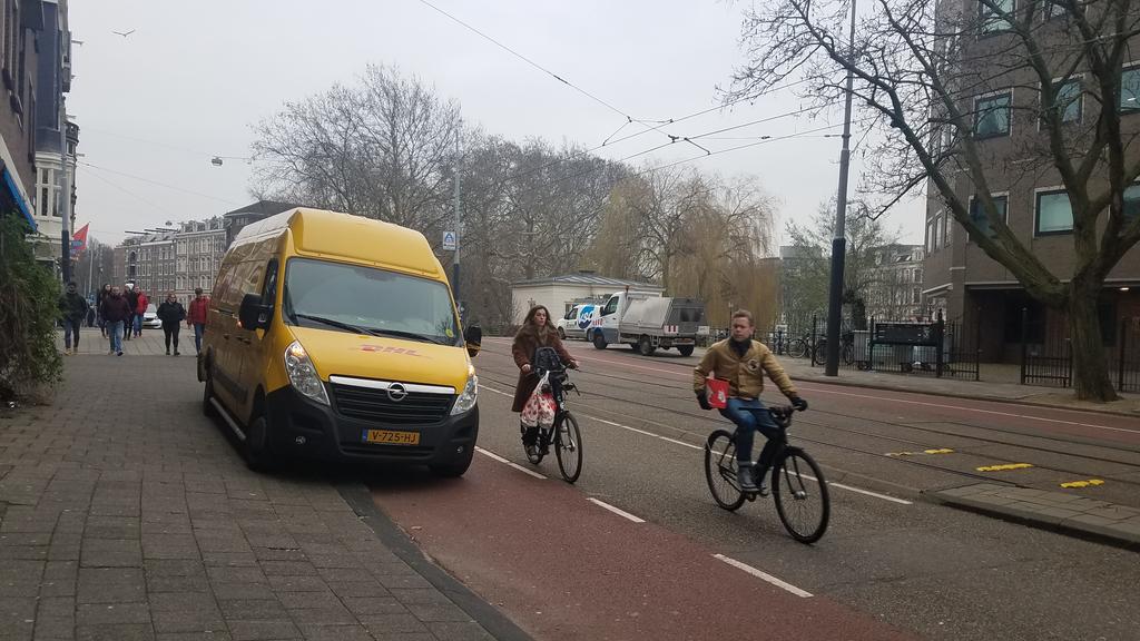 Two bikes riding around a DHL van parked in the bike lane of an Amsterdam street