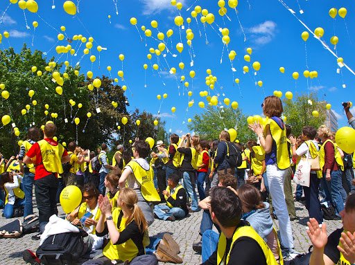 people sitting and standing, watching balloons soar in the sky. 