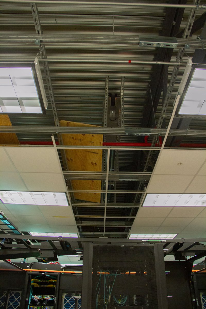 TACC's tweet photo. Busy morning in the machine room as we prepare for the Frontera supercomputer. Crews placed the transformers (white) and are building the power bus (above). https://t.co/wGKQVhodT7