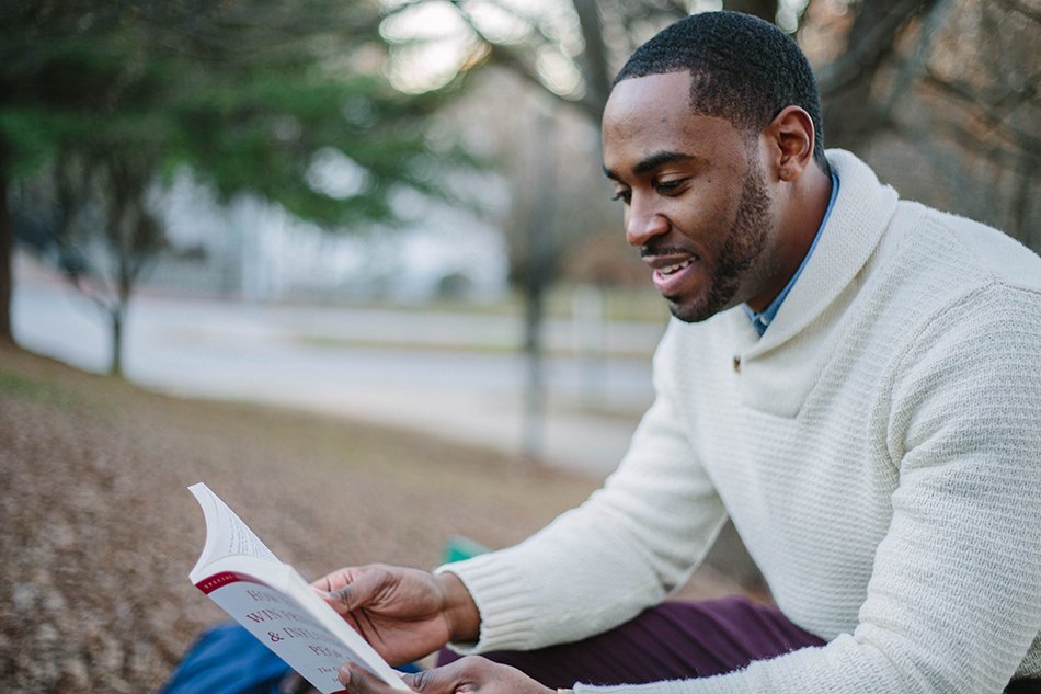 black man smiling sitting down and reading a book