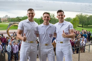 Three yell leaders gig 'em in front of the Aggie Ring statue