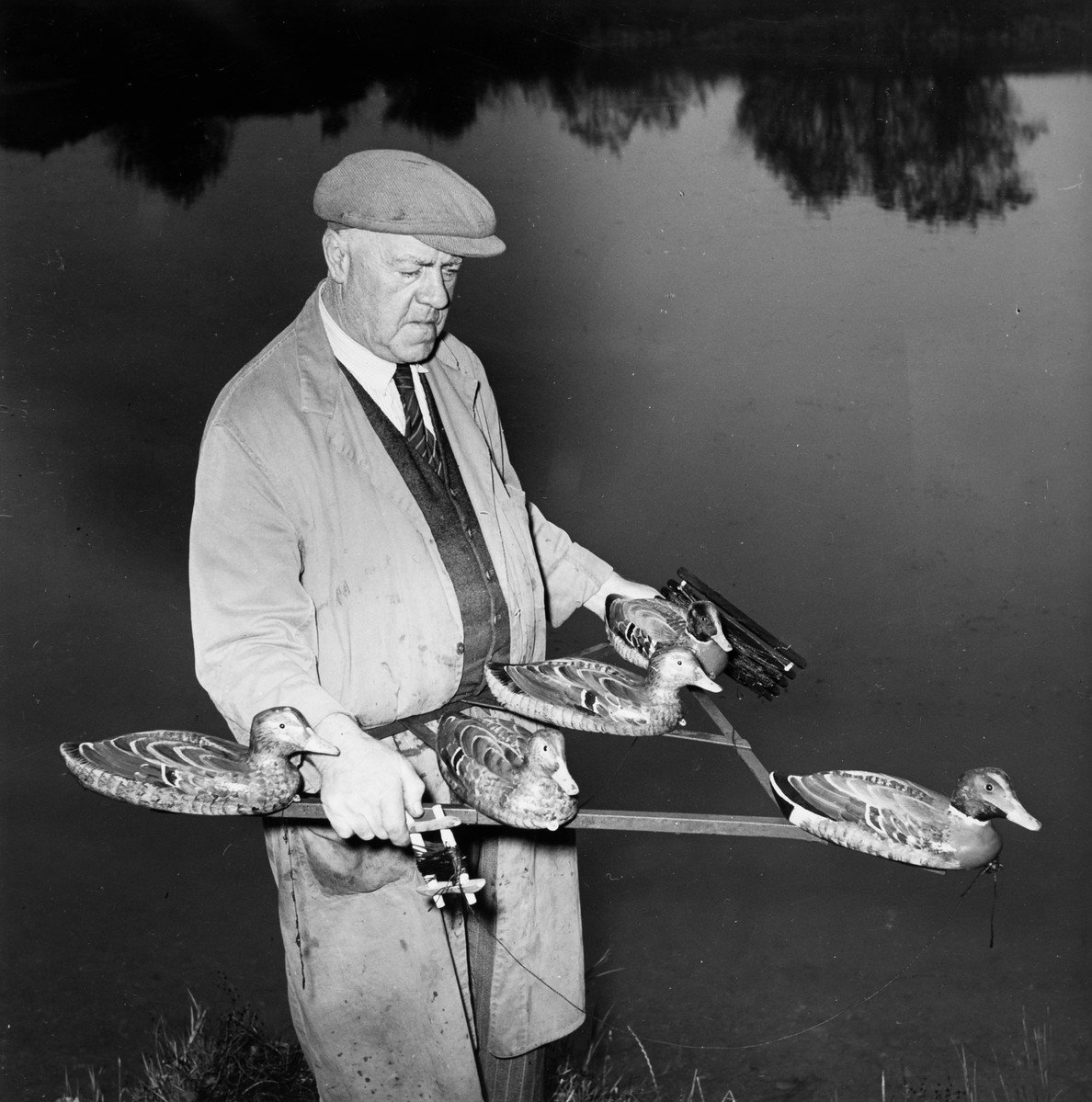 A black and white photograph of a man holding a decoy raft with wooden ducks on it.
