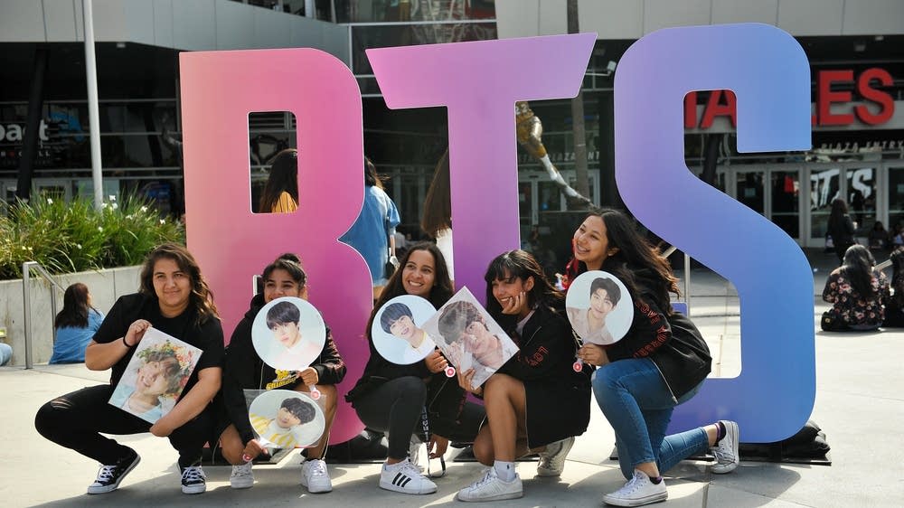 Five fans hold photos of the members of the band BTS and pose in front of the letters B-T-S at the Staples Center in Los Angeles.