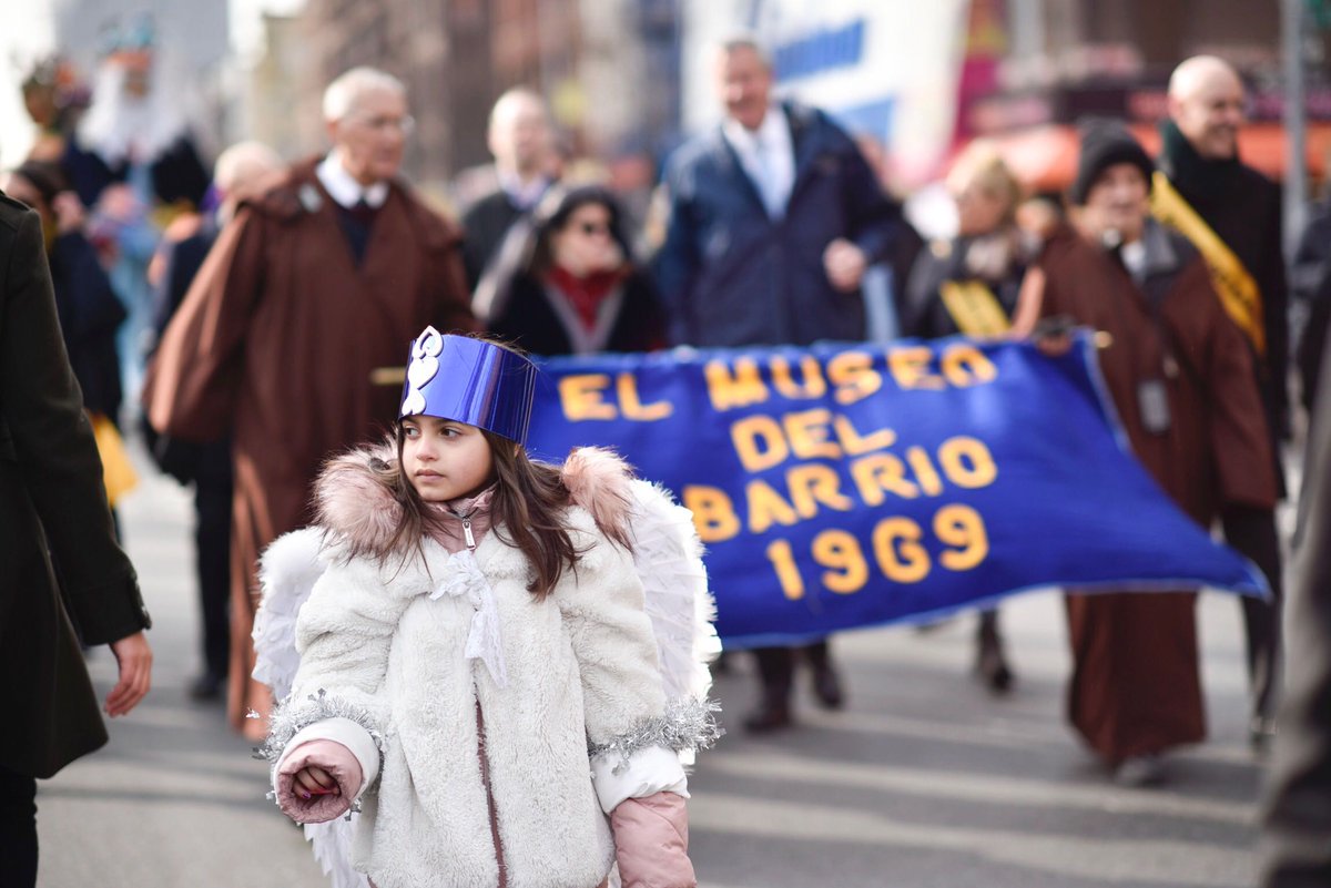 A young girl in a costume walks in front of Maor, who is walking with a banner that says "El Museo del Barrio"